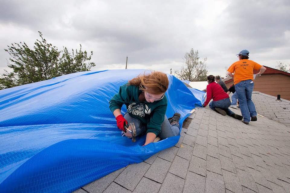 woman fixes tarp to a roof