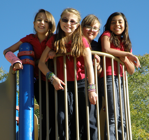 Four children standing together outside on playground equipment.