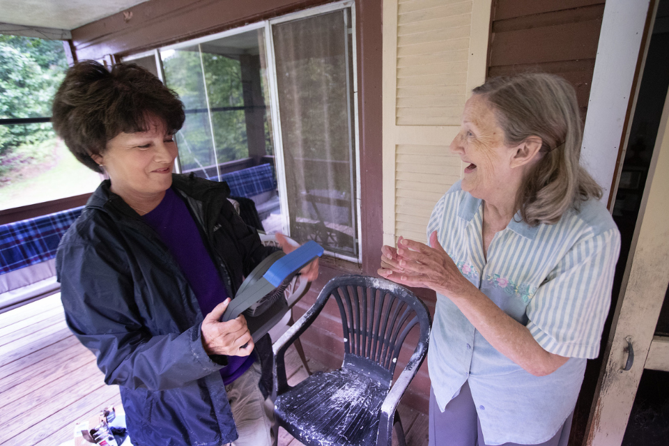 One woman giving another woman a batter-powered fan.