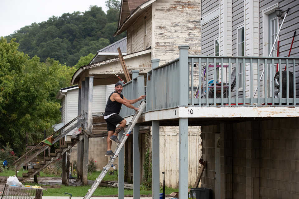 Flood survivor climbs ladder to get into his house.