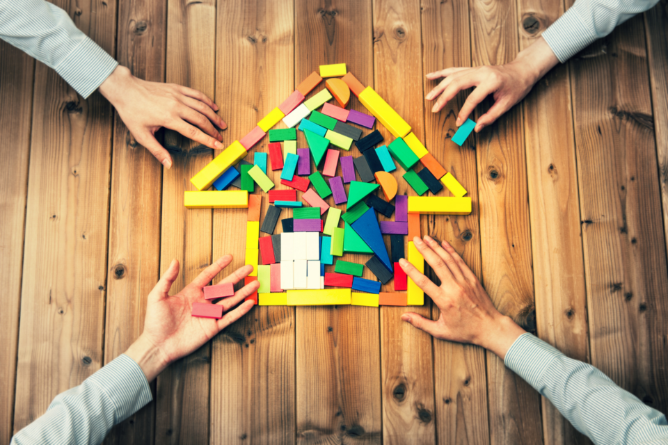 Four people making a house out of toy blocks