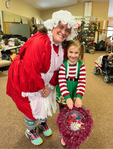 Woman dressed as Mrs. Clause and child with Christmas wreath