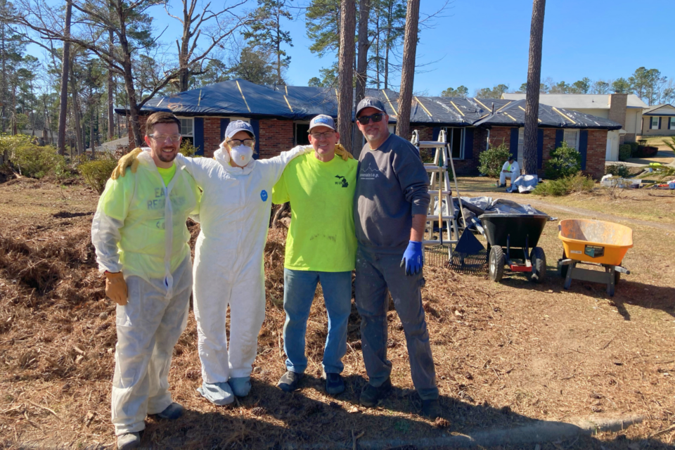 Volunteers standing in front a house that has been damaged from a hurricane