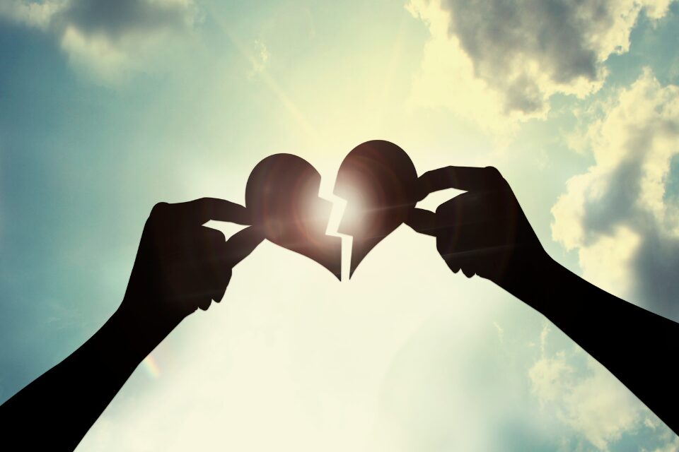 torn heard being held together by two hands with the sun streaming through the center of the torn heart