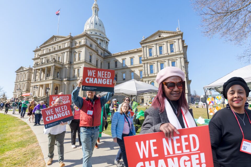 People holding signs in front of the State Capitol in Lansing